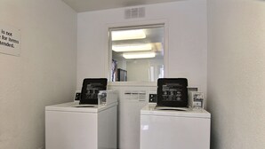 A laundry room with two white front-loading washers and dryers, a mirror above them, and a sign on the wall. - Motel 6 Bismarck, ND (Bismarck)