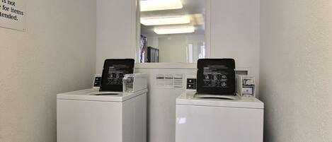 A laundry room with two white front-loading washers and dryers, a mirror above them, and a sign on the wall.