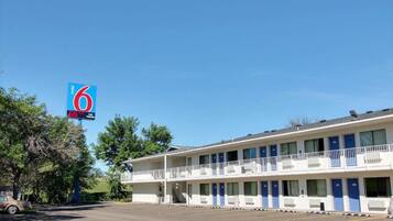 Um motel com placa azul, estacionamento e um edifício de dois andares com varandas.