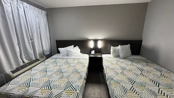 A hotel room with two single beds, a headboard with lights, a window with curtains, and a wall-mounted heater.