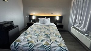 A hotel room with a bed, bedside tables, a desk, and an air conditioning unit. - Motel 6 Bismarck, ND (Bismarck)