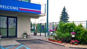 A building entrance with a 'WELCOME' sign, a gated area with potted plants, and a clear sky. - Motel 6 Bismarck, ND (Bismarck)