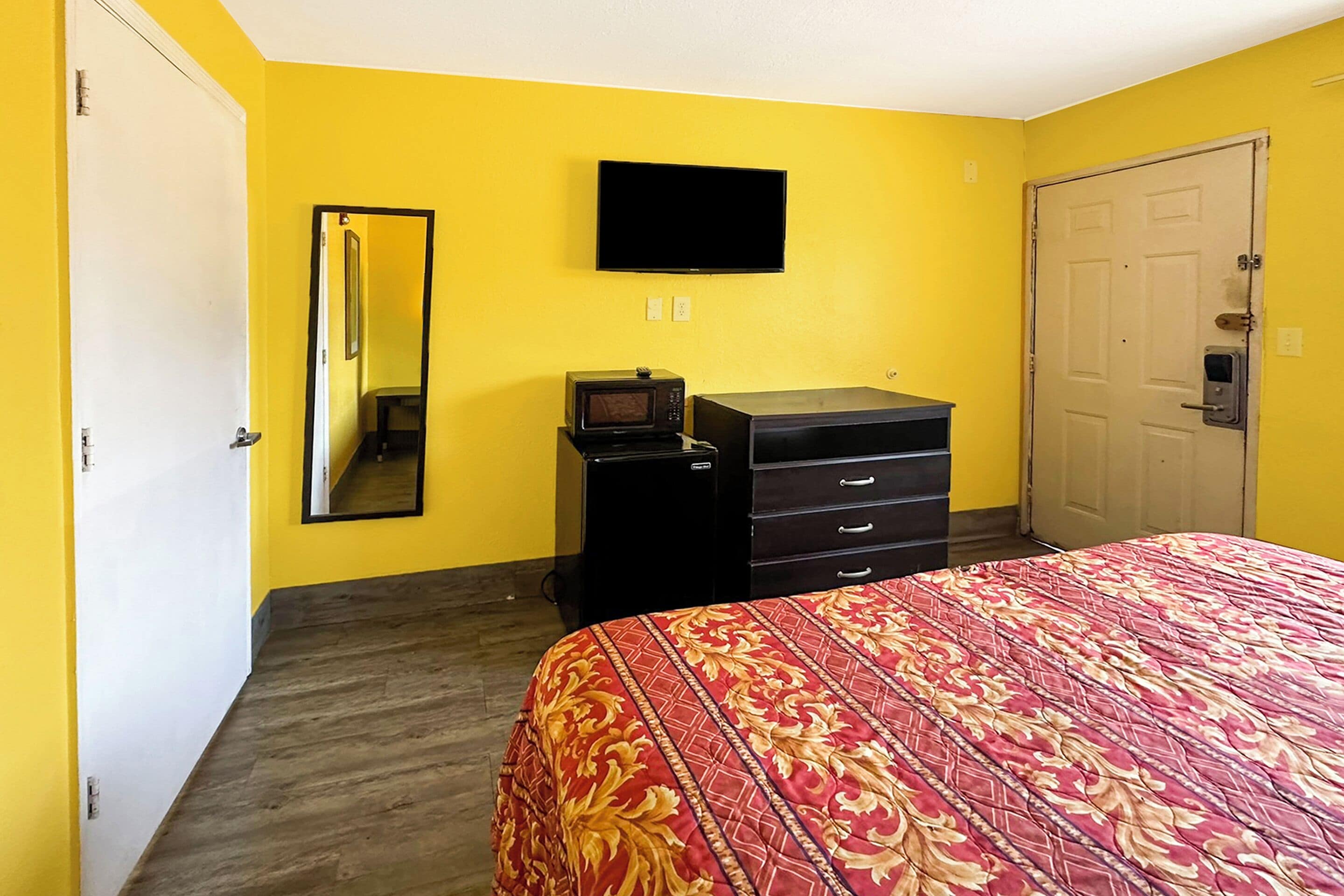A room with a bed, a dresser, a television, and a door.