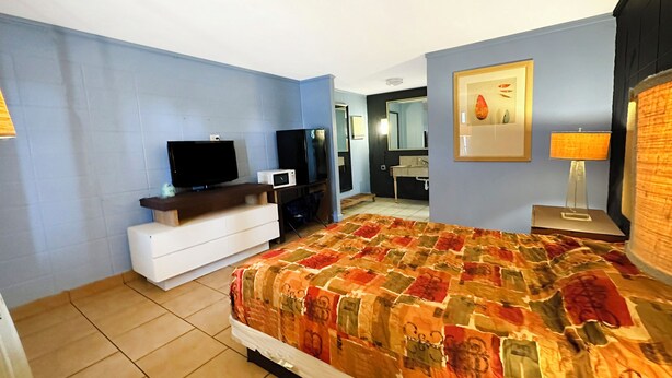 A hotel room with a bed, a TV, a microwave, a dresser, a bathroom with a mirror, and a painting on the wall. - Luxury Inn by OYO Albany (Albany)