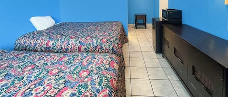 A room with two beds, a small table, a dresser, and a wall-mounted lamp.