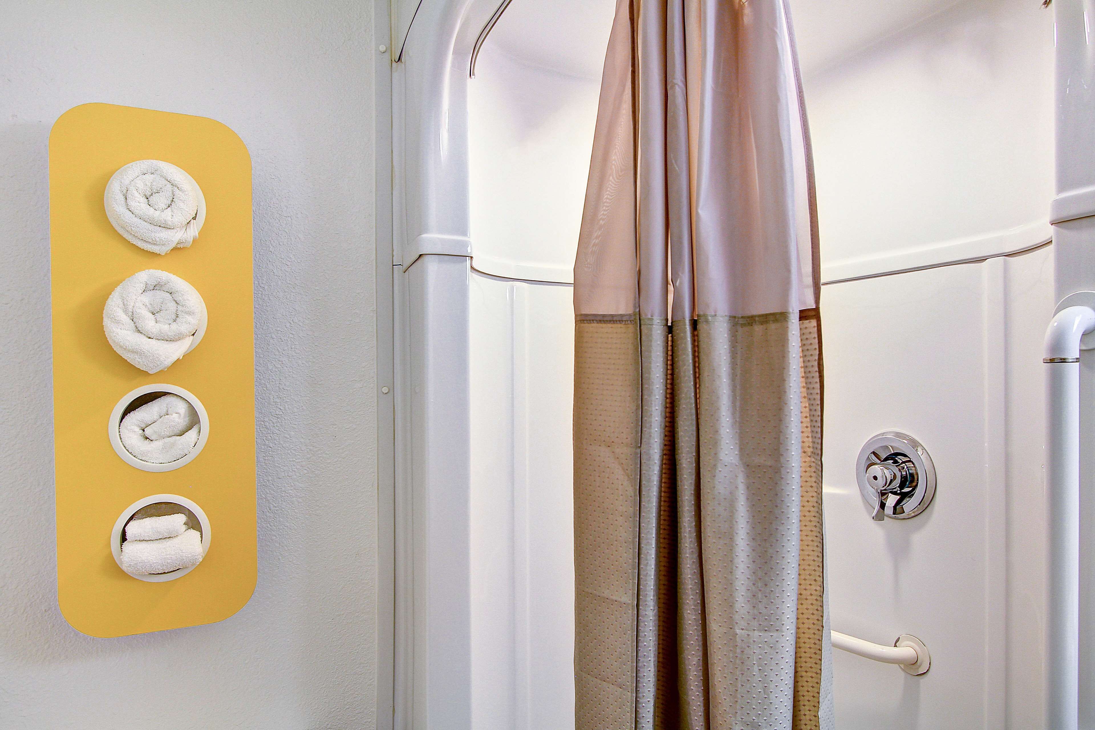 Un baño con un toallero amarillo que sostiene cuatro toallas, una cortina de ducha y un grifo blanco.