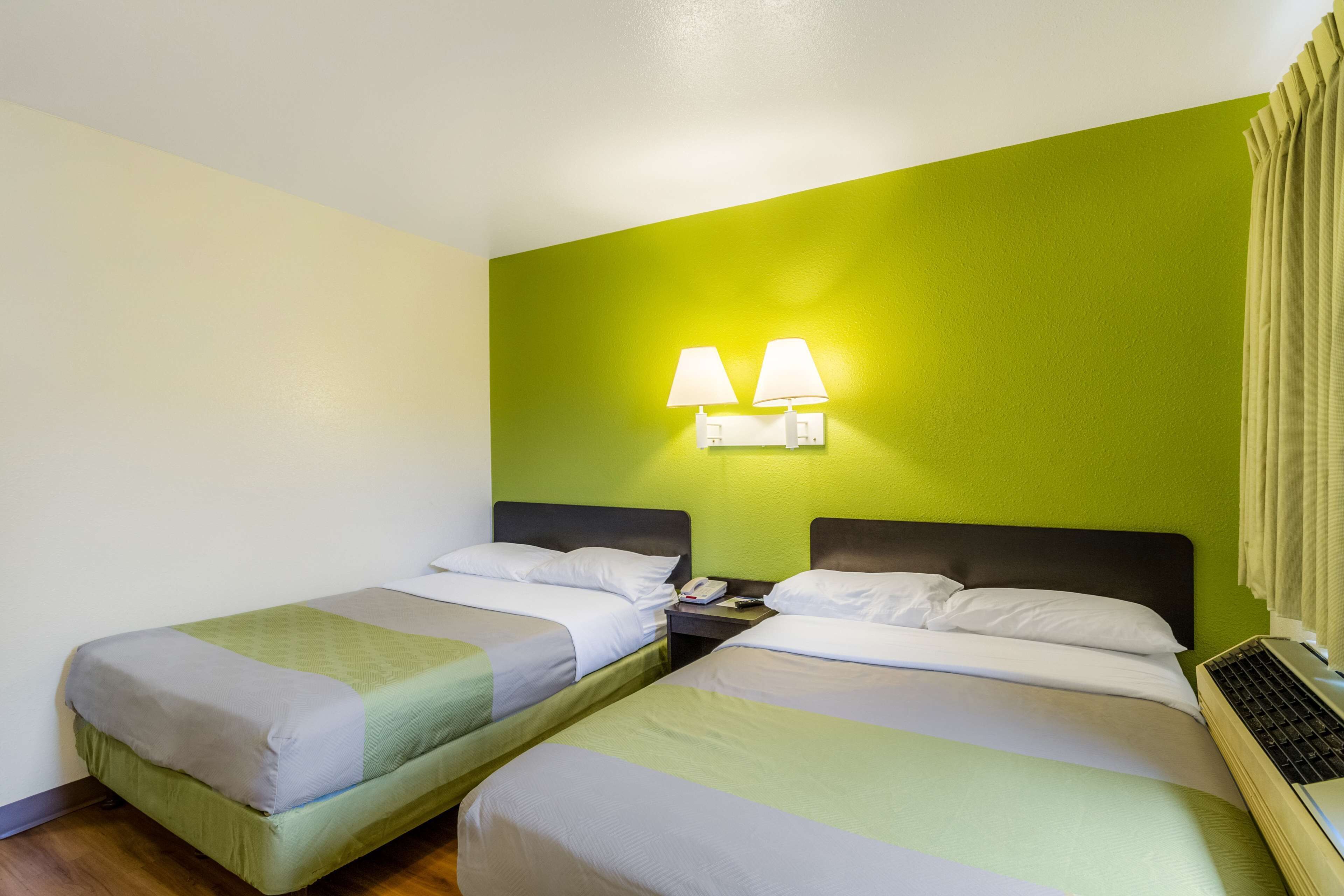 Habitación de hotel con dos camas individuales, una mesita de noche con teléfono y lámpara, y una ventana con cortinas.