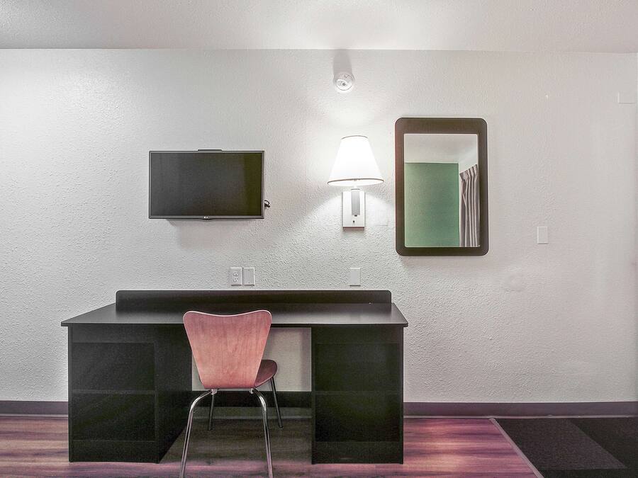 A small, modern bathroom with a dark vanity, a pink chair, a wall-mounted TV, a mirror, and a light fixture.