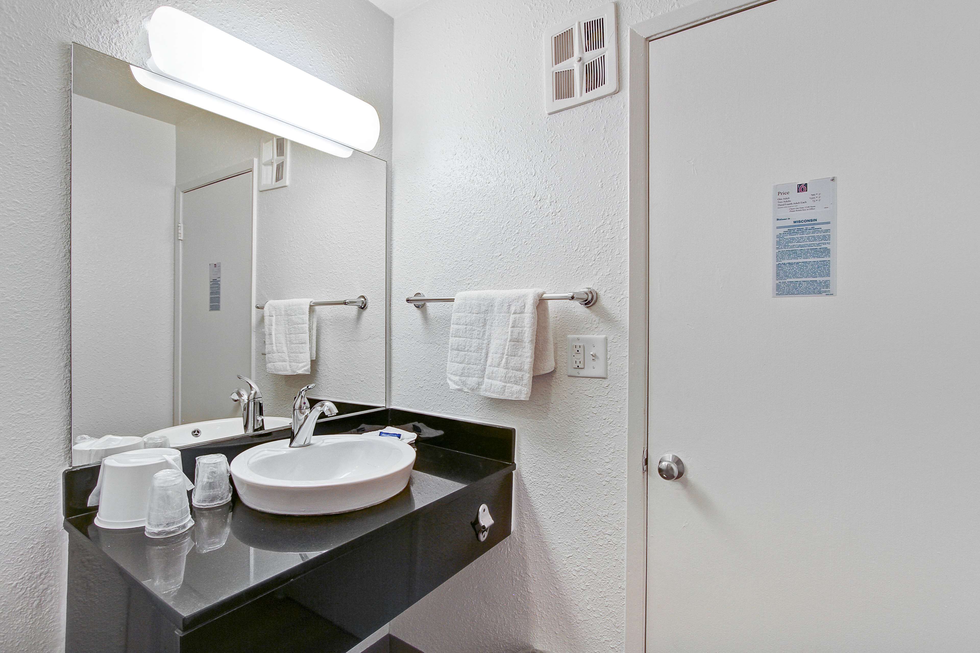 A bathroom with a white sink, black countertop, and a mirror. There are two white towels hanging on towel bars.