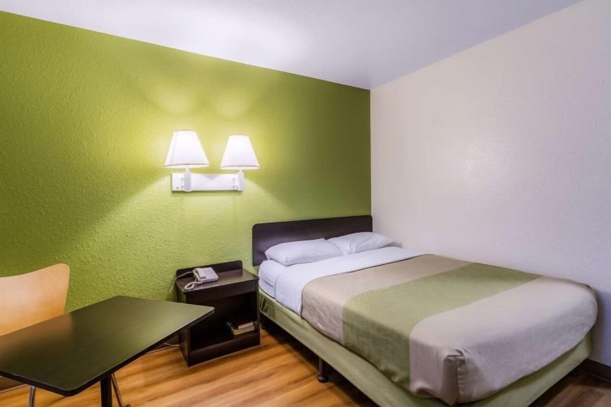 Een enkel bed met een groene muur en een wit plafond, een nachtkastje met een lamp, en een houten vloer.