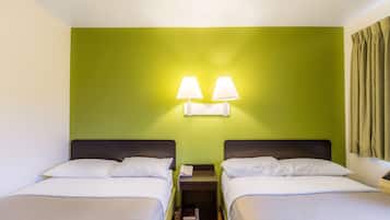 Una habitación de hotel con dos camas, una mesita de noche con una lámpara y una pared verde.