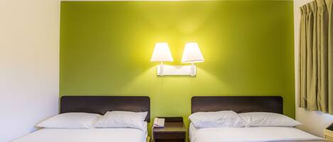 Una habitación de hotel con dos camas, una mesita de noche con una lámpara y una pared verde.