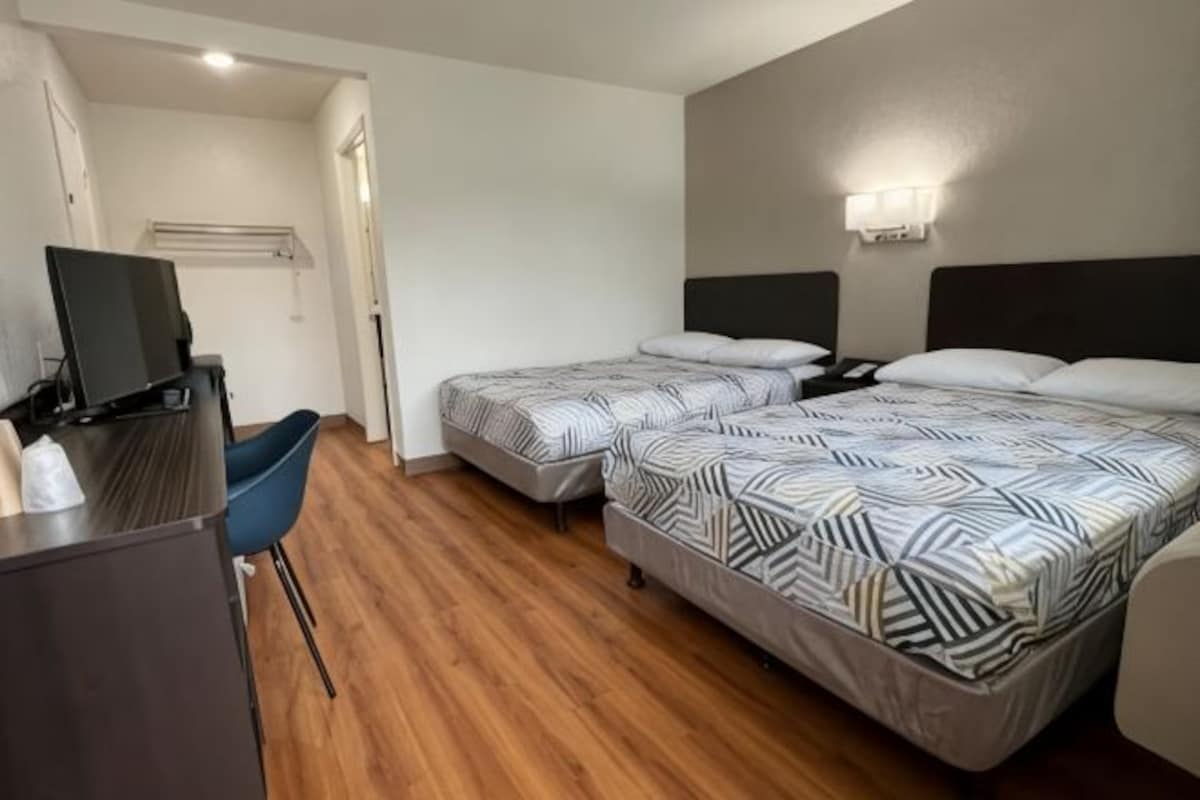 A hotel room with two beds, a desk with a computer, and a chair.