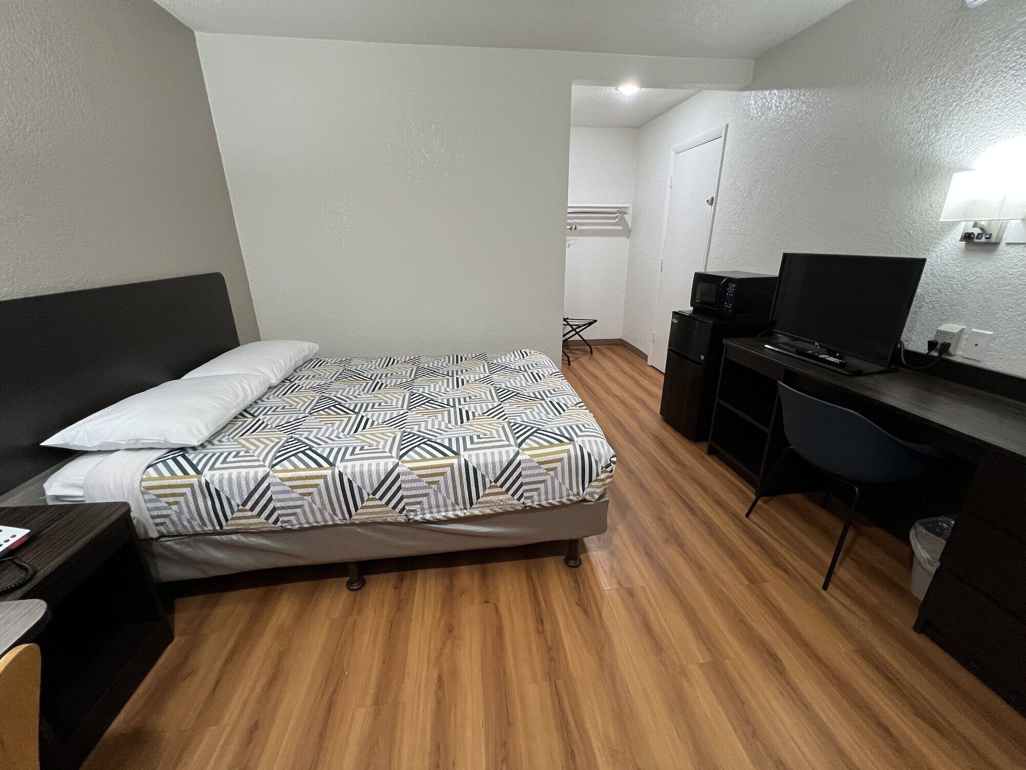 Ein Schlafzimmer mit einem Bett, einem Schreibtisch, einem Sessel, einem Fernseher und einer Mikrowelle.