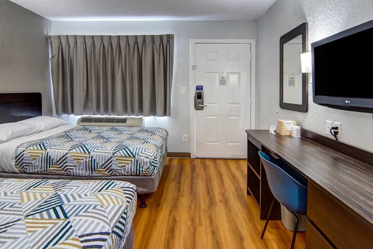 A hotel room with two beds, a desk, a chair, a television, and a door.