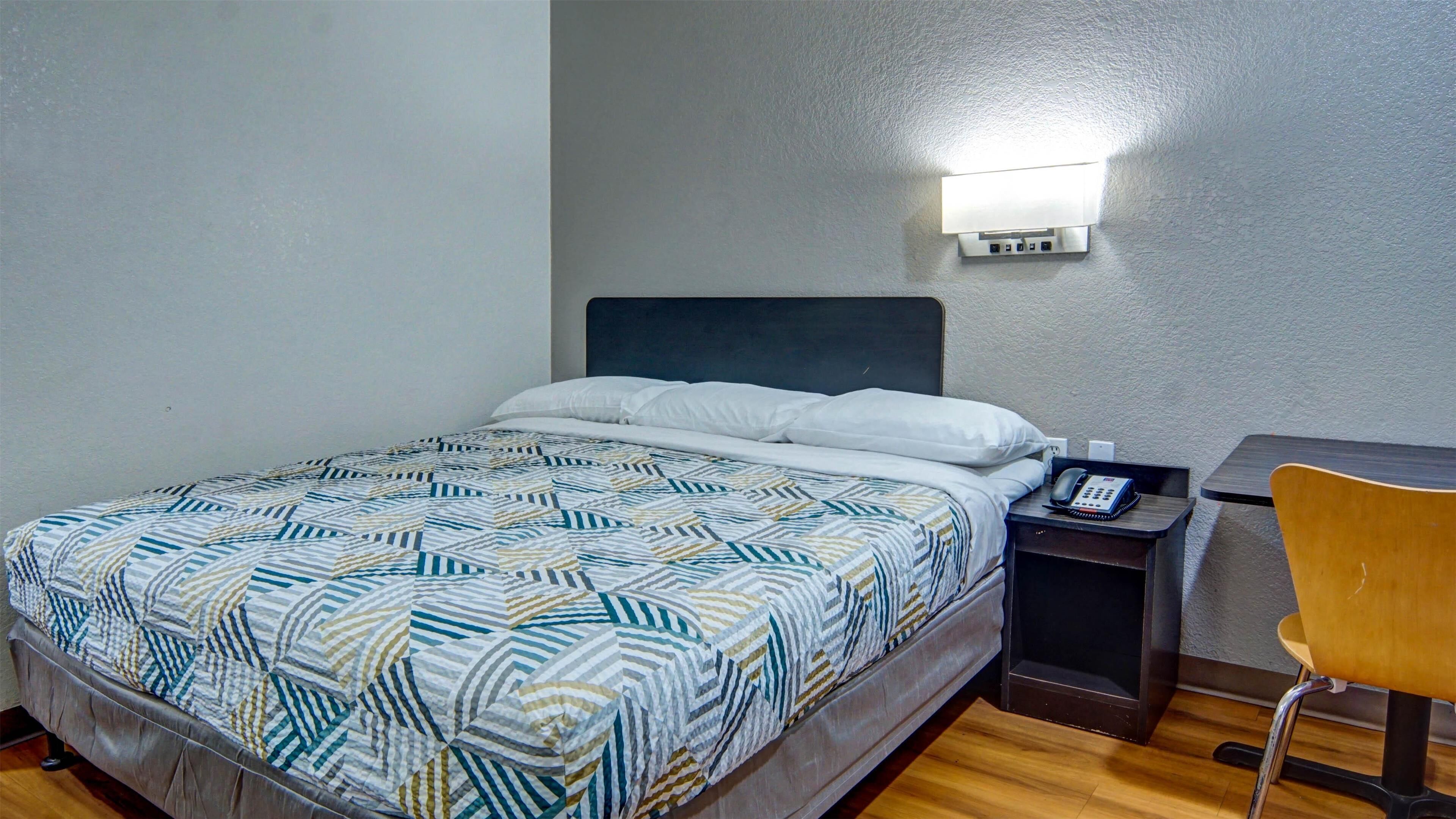 Une chambre d’hôtel avec un lit, une table de chevet avec un téléphone, une chaise et une lampe fixée au mur.
