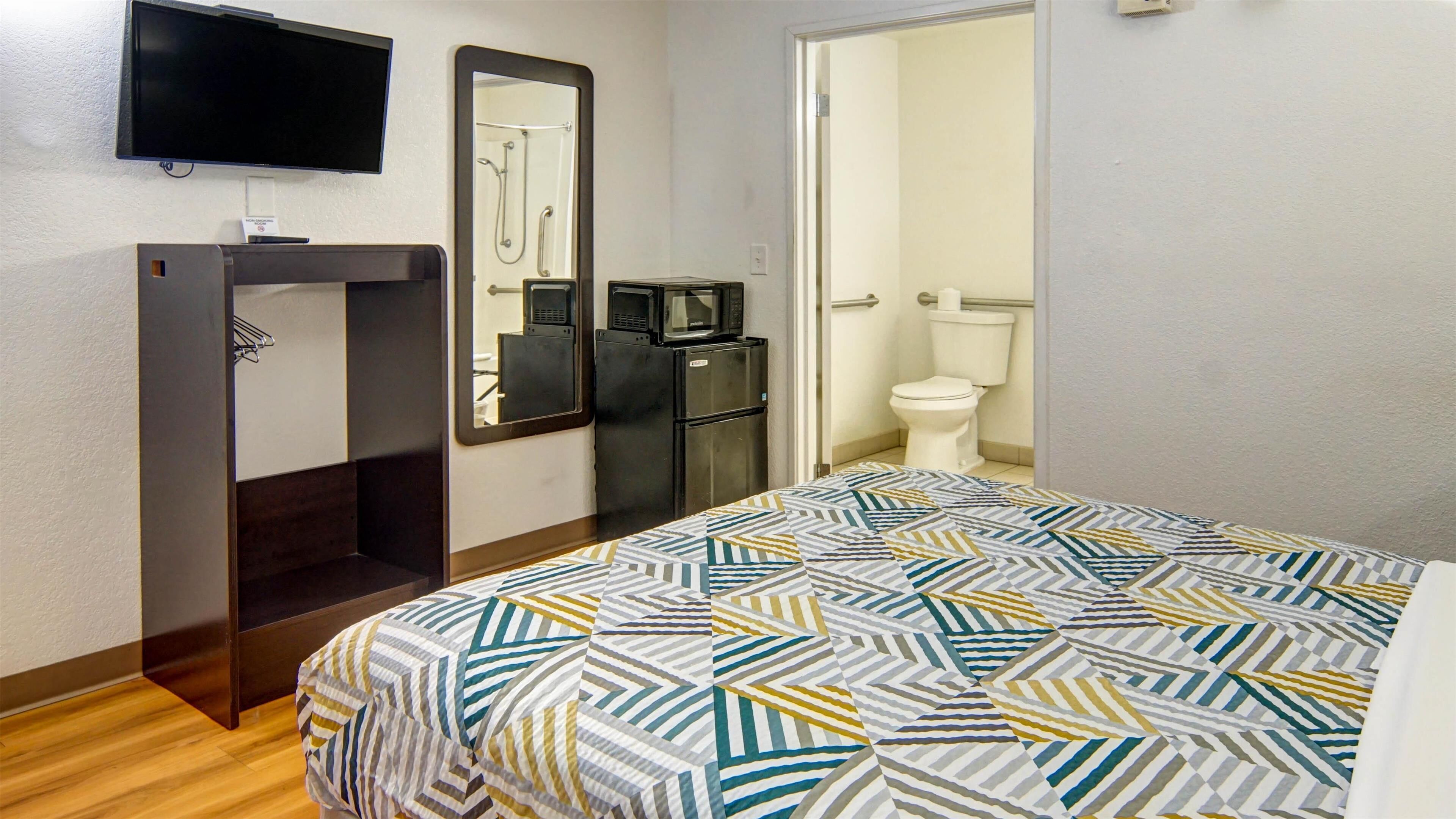 Une chambre à coucher comprenant un lit, un téléviseur fixé au mur, un réfrigérateur et des toilettes.