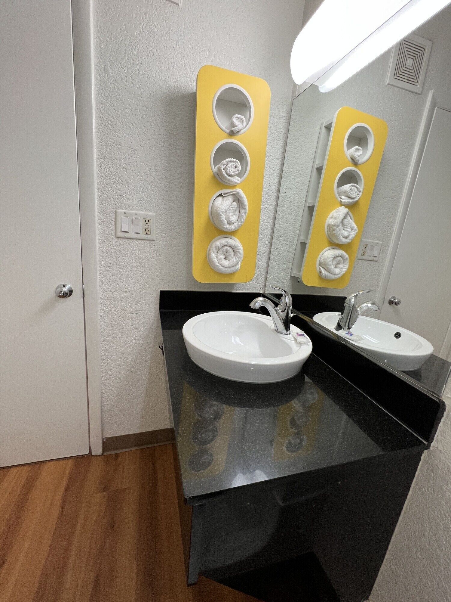 A bathroom with two sinks, a mirror, and a towel rack with five towels.