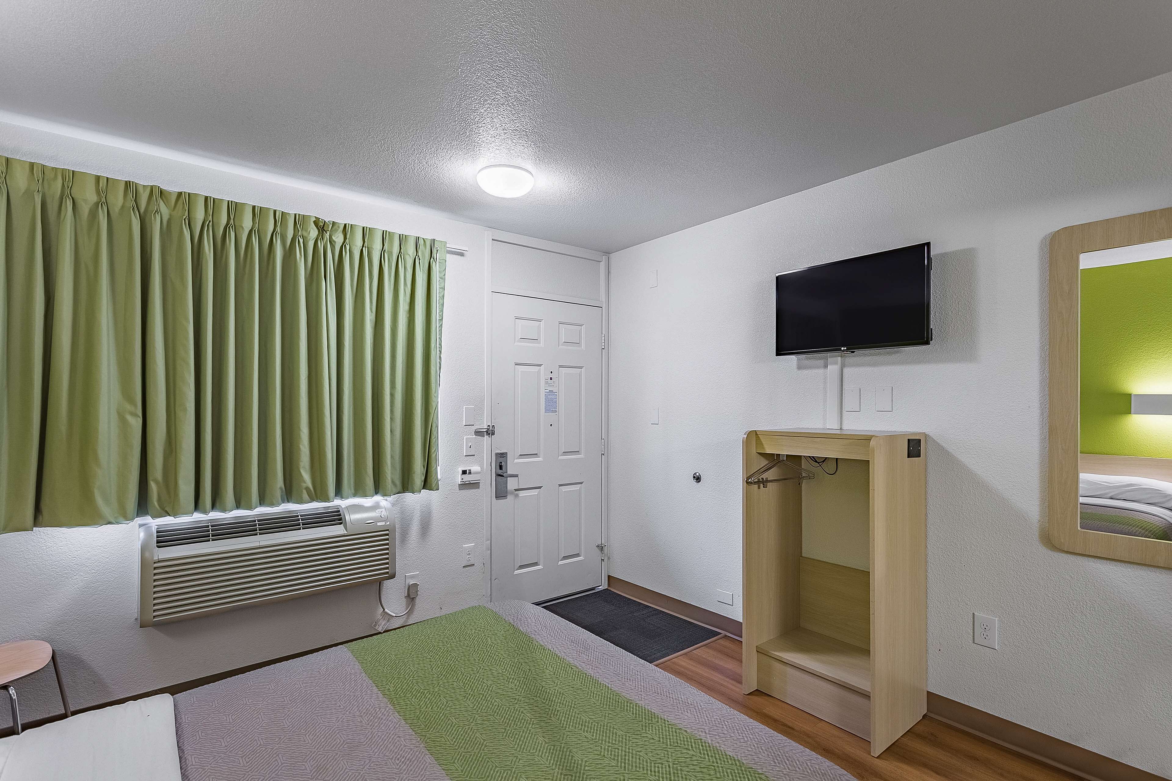 A room with a bed, a bedside table, a TV mounted on the wall, and a window with curtains.