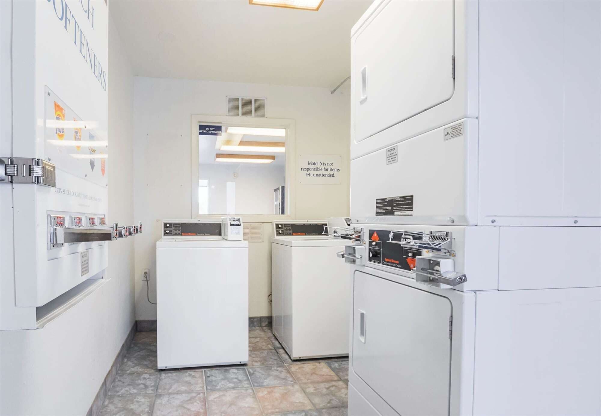 A laundry facility with multiple washing machines and dryers, a sign indicating responsibility for items left unattended, and a tiled floor.
