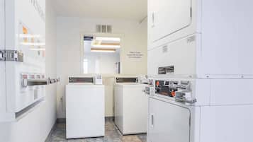A laundry facility with multiple washing machines and dryers, a sign indicating responsibility for items left unattended, and a tiled floor.