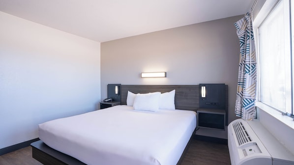 A hotel room with a large bed, bedside tables, a wall-mounted light, and a window with curtains.