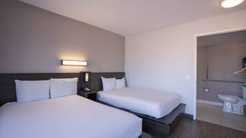 Una habitación de hotel con dos camas, una mesita de noche con lámpara, y un baño con inodoro y ducha.
