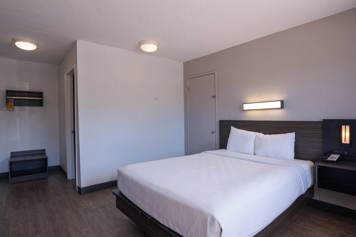 A hotel room with a large bed, bedside tables, a flat-screen TV, and a wall-mounted light.