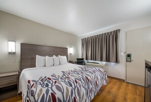A hotel room with a large bed, a desk, an air conditioning unit, and a door.