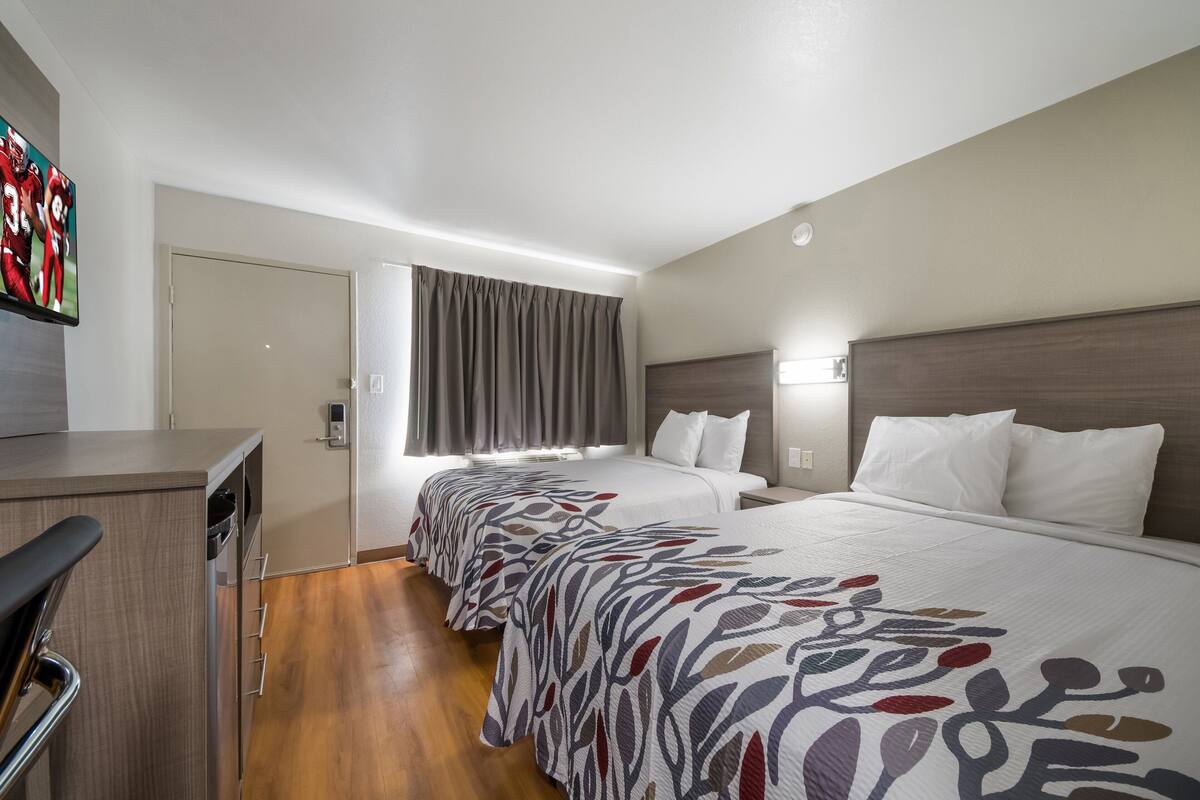 A hotel room with two beds, a desk, and a TV.