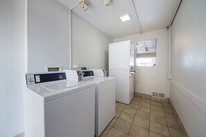 A laundry room with two washing machines, a dryer, and a small window.