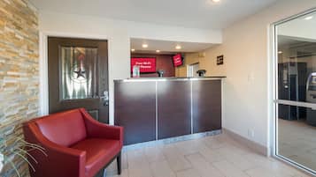 A reception area with a red chair, a reception desk, a digital screen, and a glass door leading to a room.