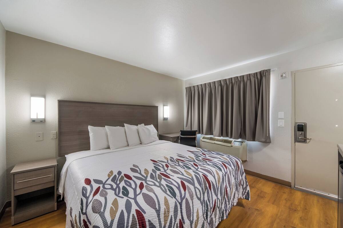 A hotel room with a large bed, bedside tables, a desk, and a window with curtains.