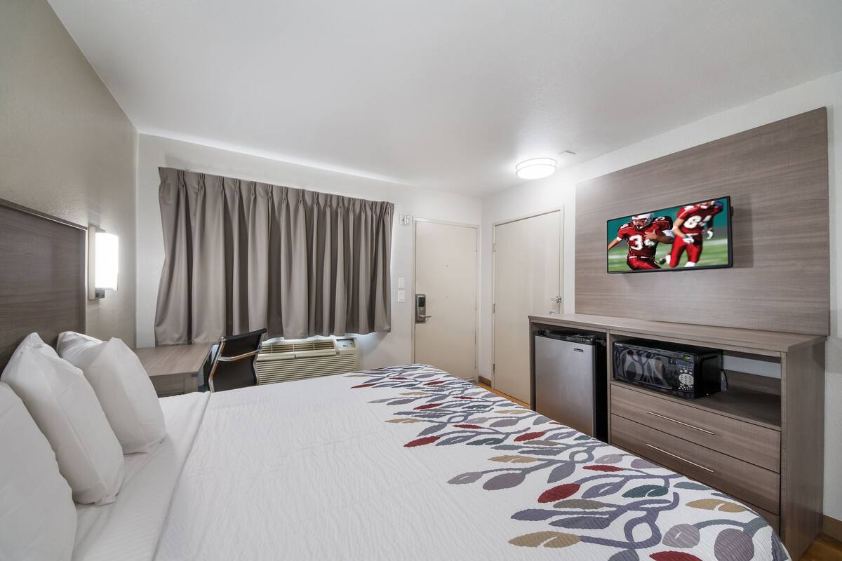 A hotel room with a bed, a TV on the wall, a desk, and a microwave.