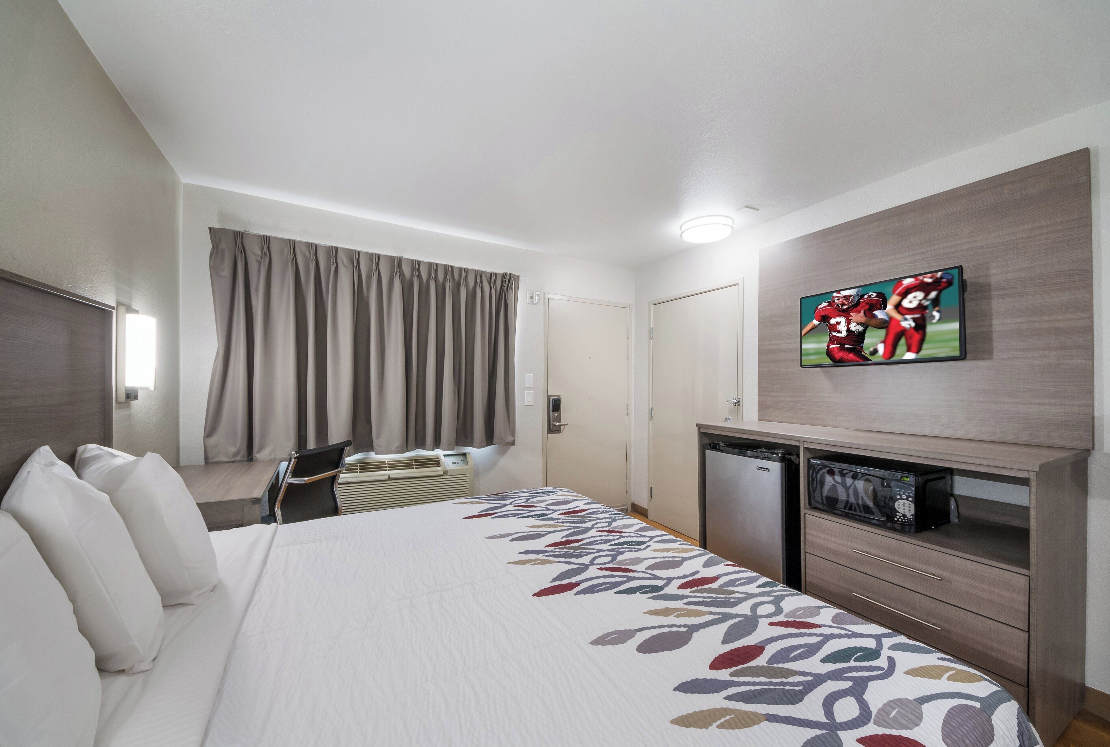 Une chambre d’hôtel équipée d’un lit, d’un bureau, d’une chaise, d’une télévision, d’un four à micro-ondes et d’une armoire.