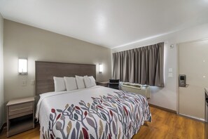 A hotel room with a bed, bedside tables, a desk, an air conditioning unit, and a wardrobe.
