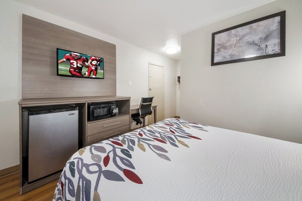A hotel room with a bed, a television mounted on the wall, a small refrigerator, and a door. - Red Roof Inn San Antonio E – Frost Bank Center (San Antonio)