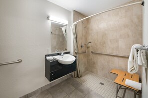 A bathroom with a sink, mirror, shower, and a wooden bench.