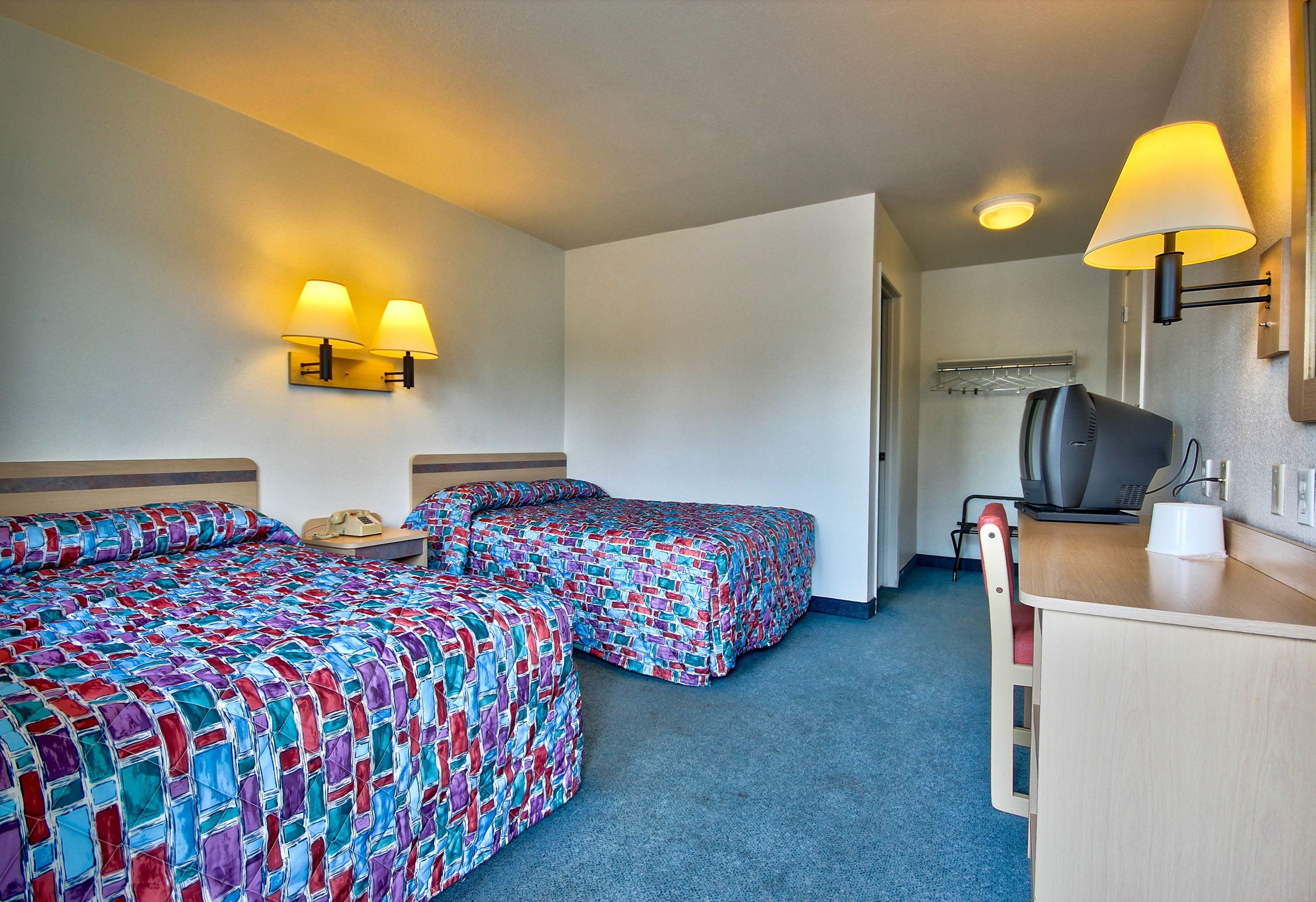 A hotel room with two beds, a desk, a chair, and a television.