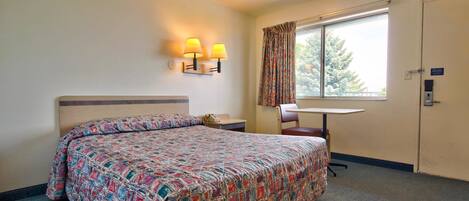 Una habitación de hotel con una cama, un escritorio, una silla y una ventana con cortinas.