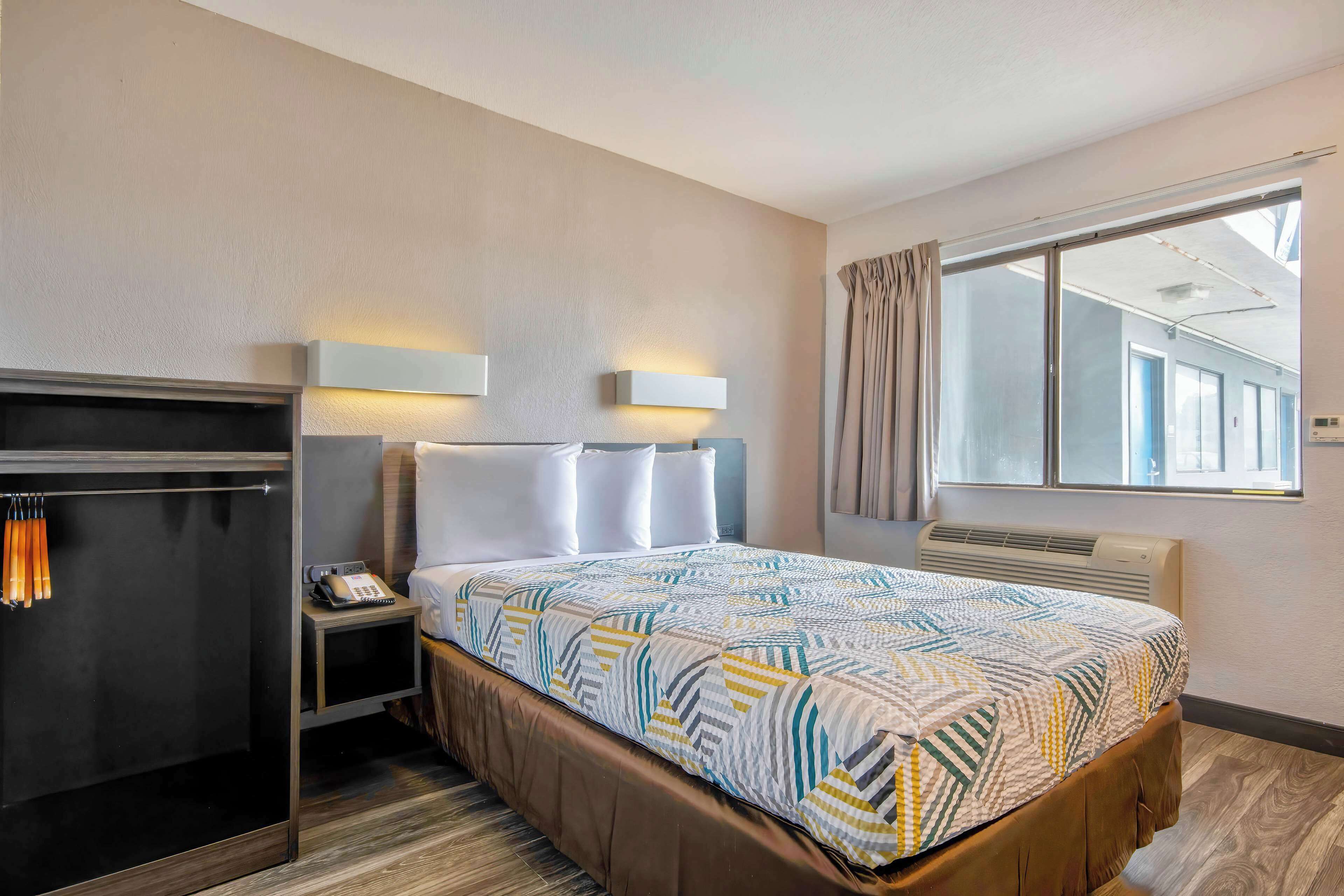 A hotel room with a bed, a wardrobe, a bedside table with a phone, and a window with curtains.