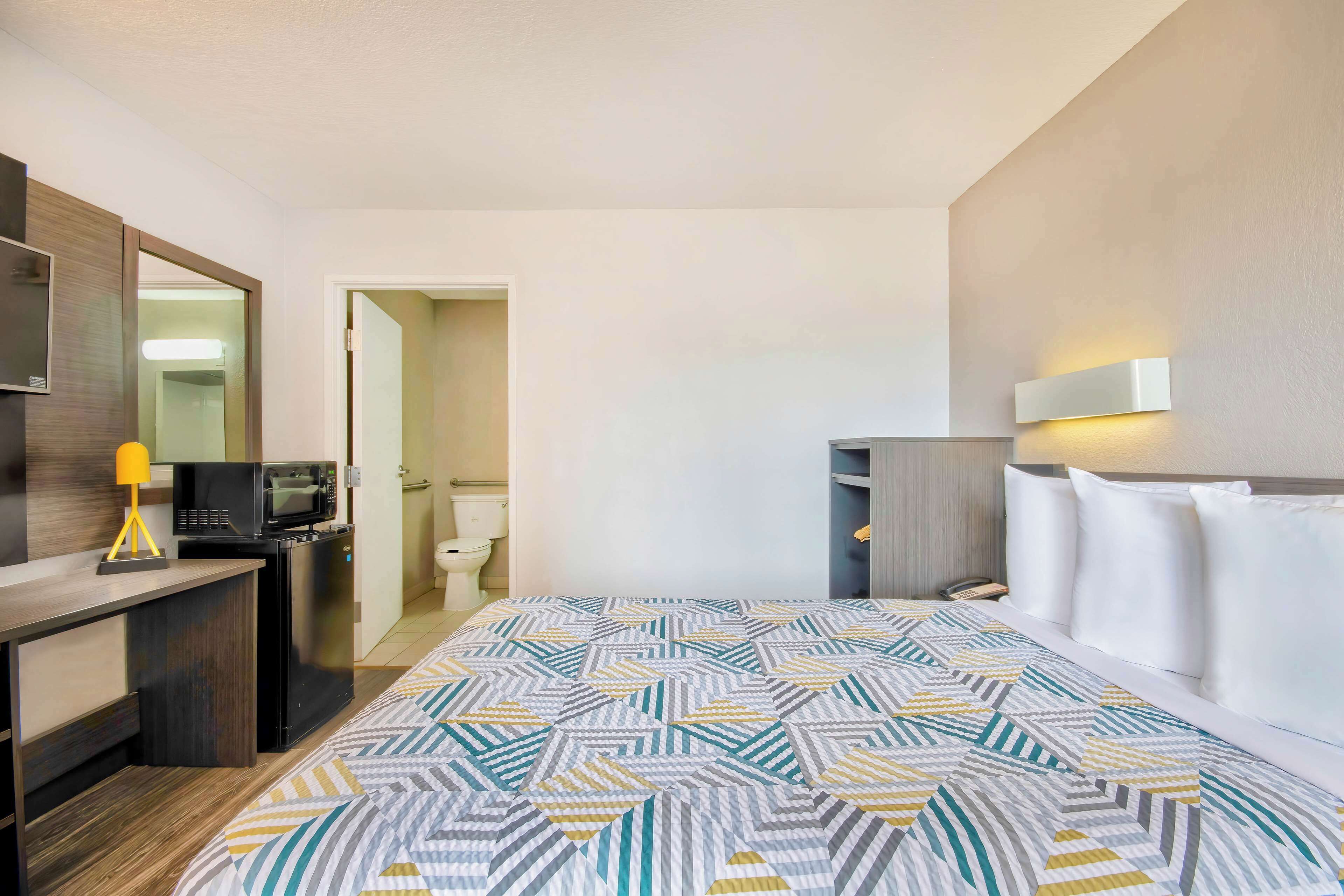 Una habitación de hotel con cama, escritorio, microondas, teléfono y mesita de noche.
