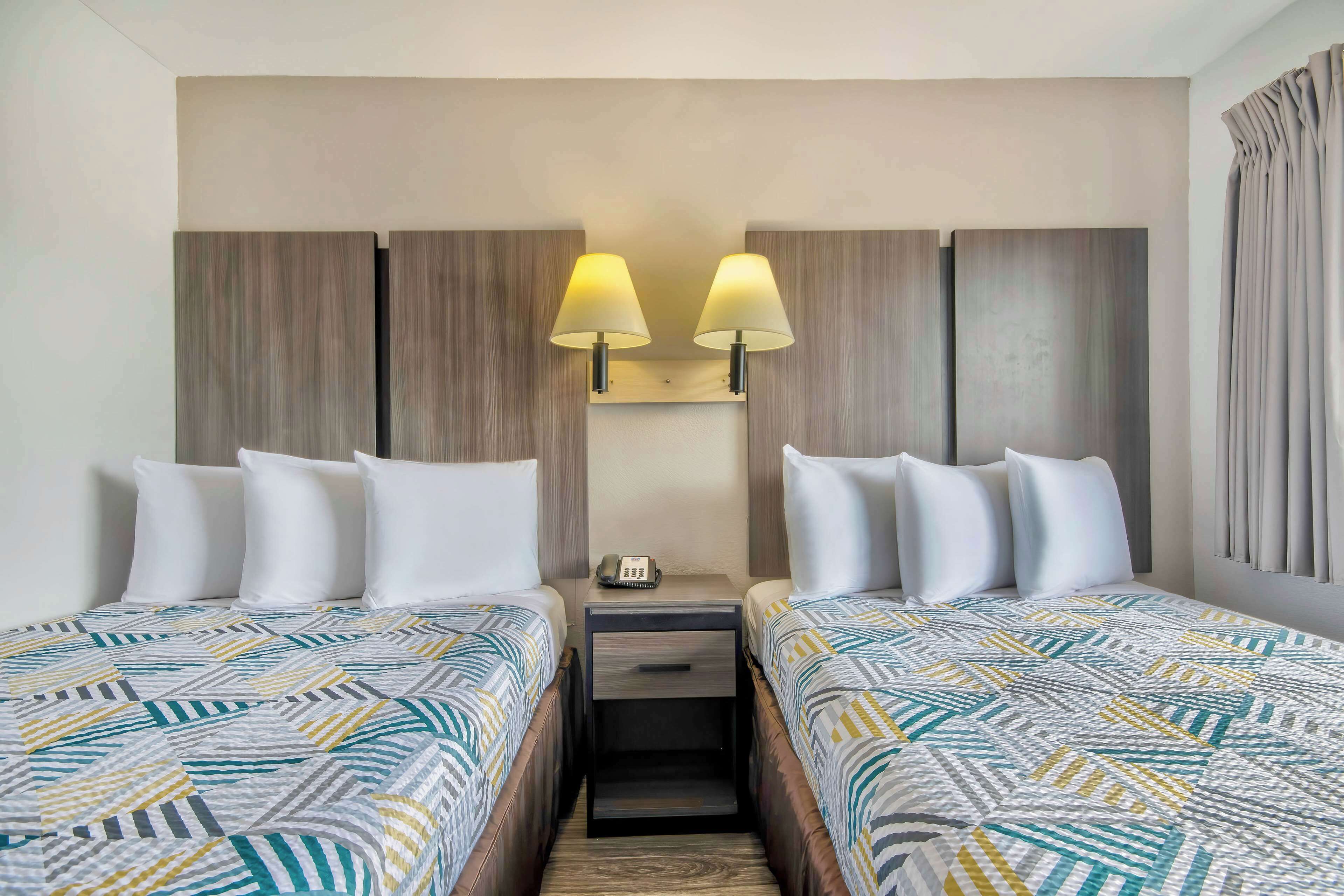 A hotel room with two beds, a nightstand with a phone, and two wall-mounted lamps.