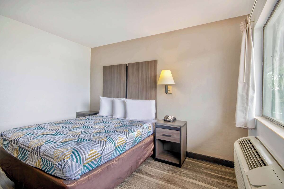 A hotel room with a bed, a nightstand, a lamp, and a window with curtains.