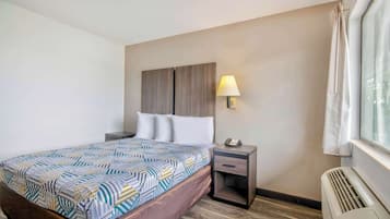 A hotel room with a bed, a nightstand, a lamp, and a window with curtains.