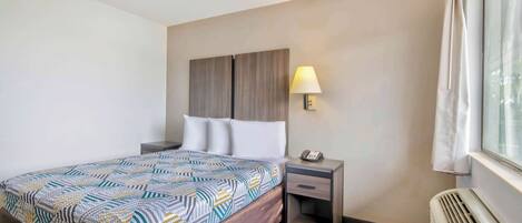 A hotel room with a bed, a nightstand, a lamp, and a window with curtains.