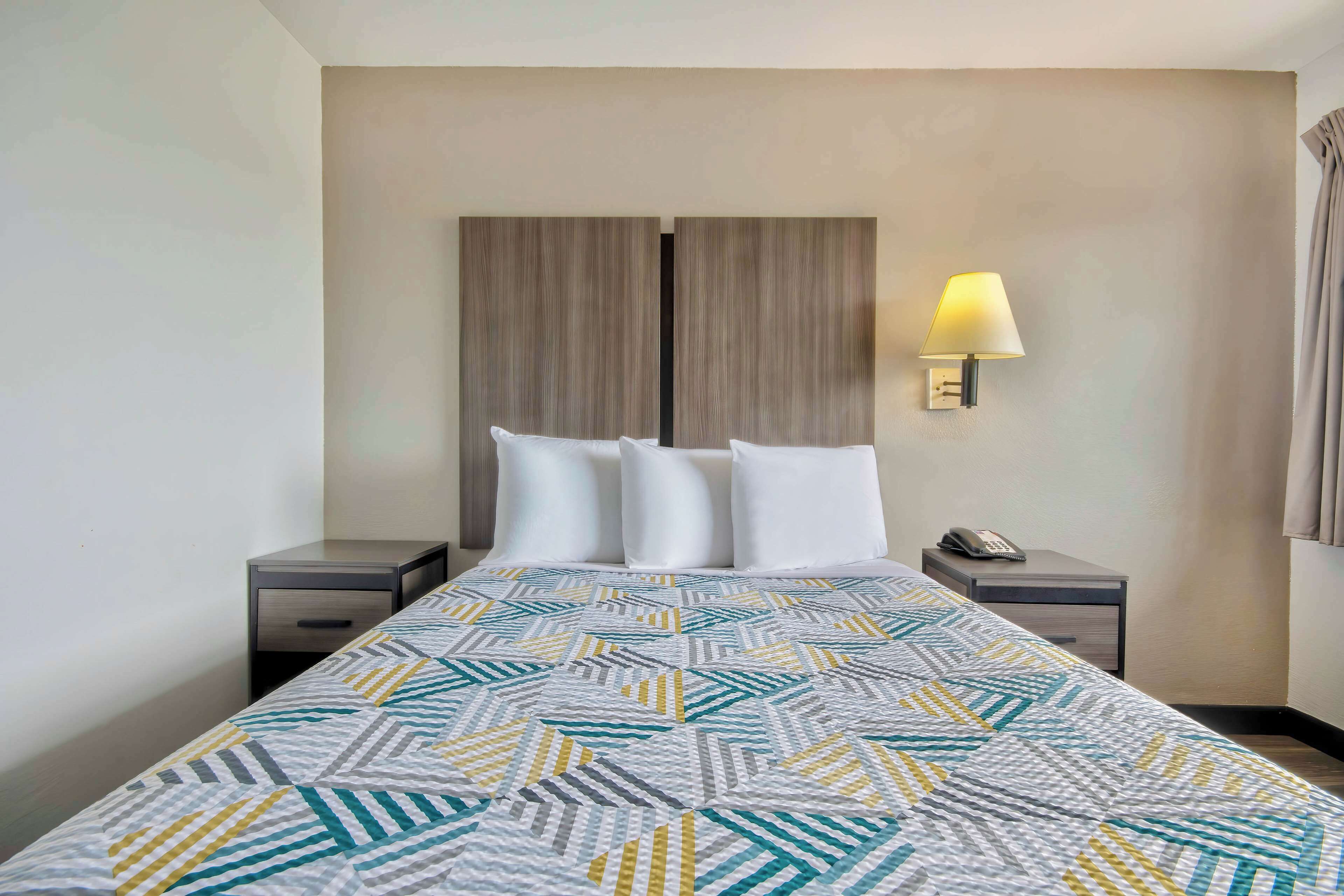 A hotel room with a bed, two nightstands, a lamp, and a wall-mounted phone.