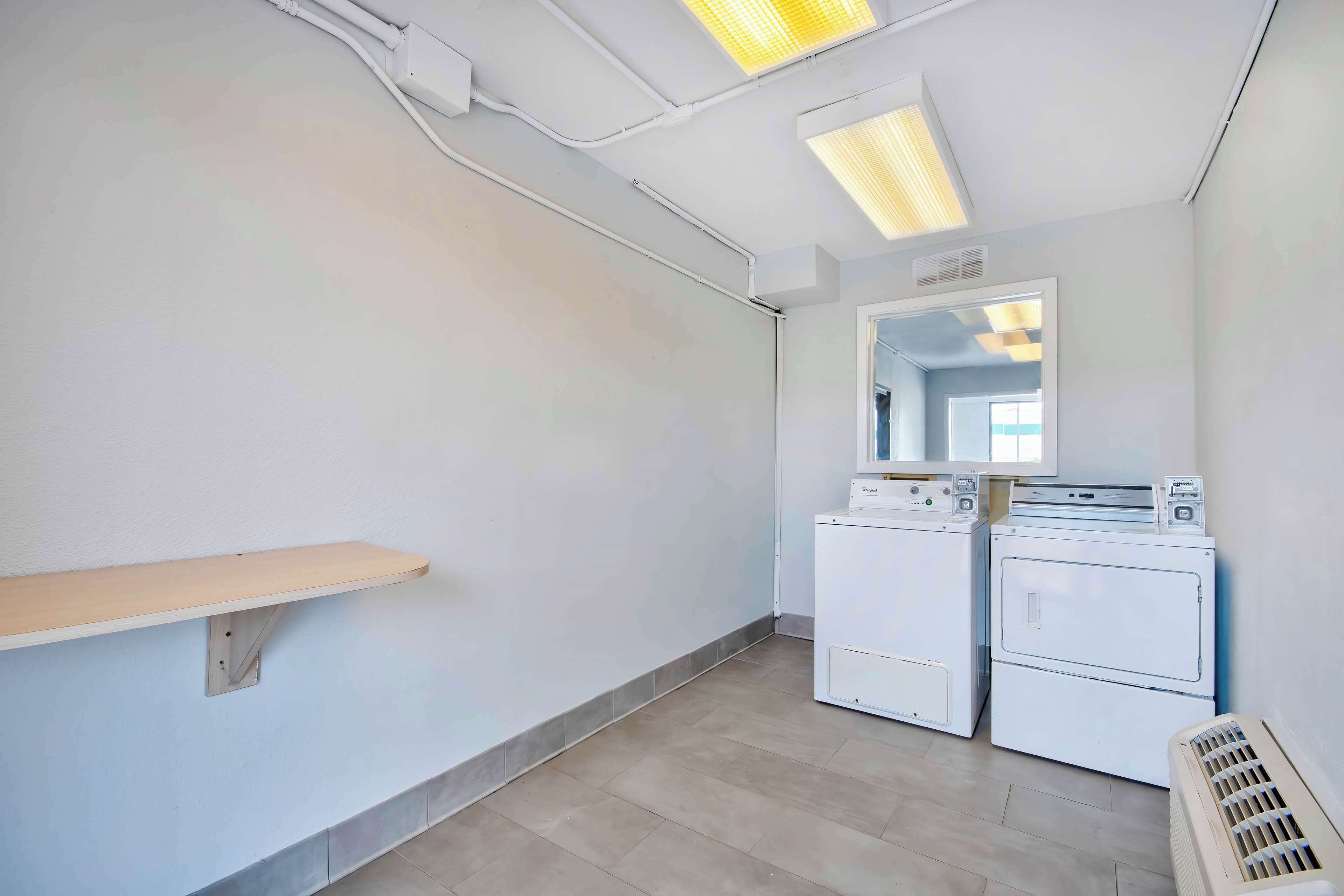 A laundry room with two washing machines, a drying machine, a vent, and a shelf.