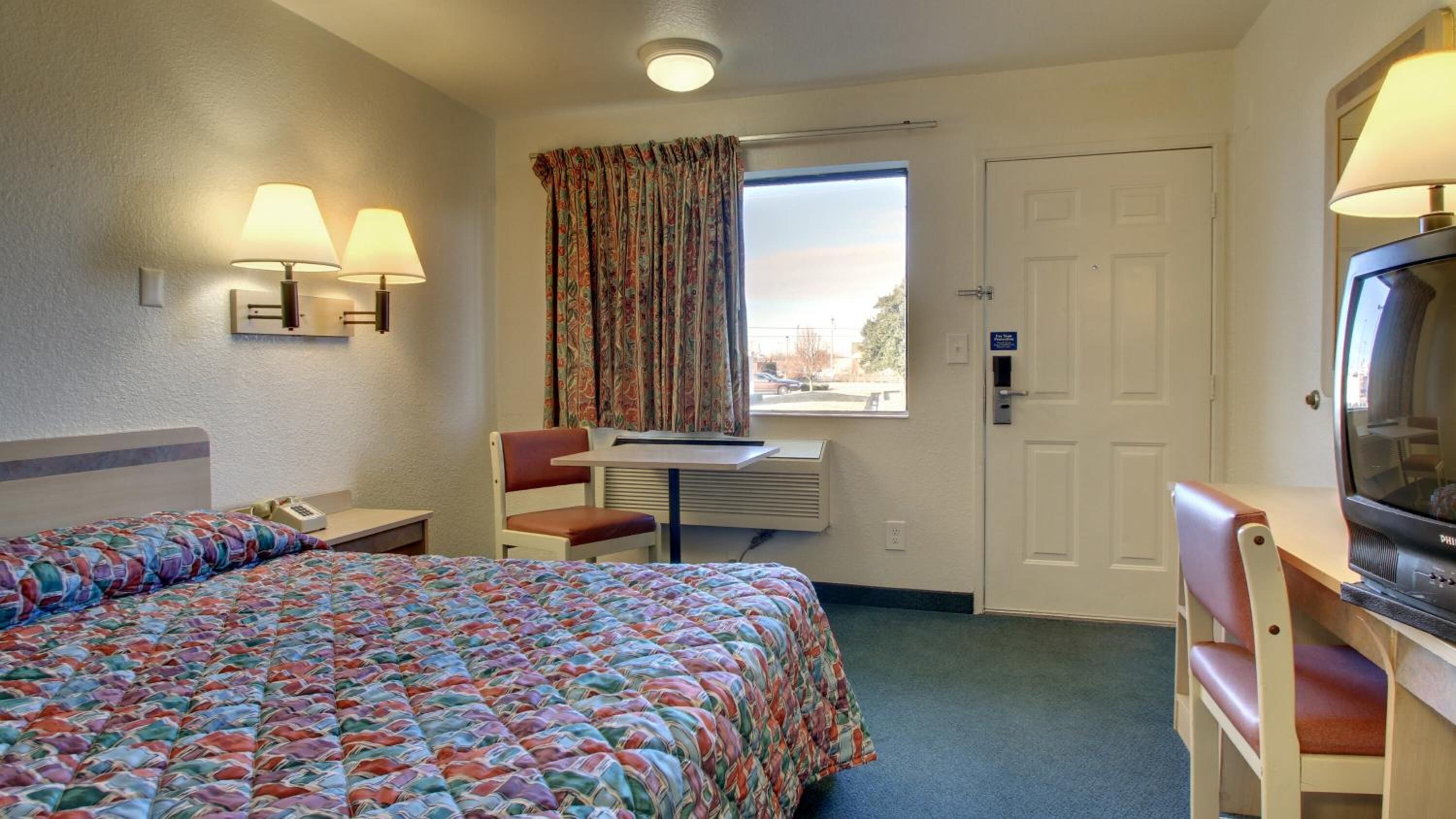 Habitación de hotel con dos camas, un escritorio con silla, televisión y ventana con cortinas.