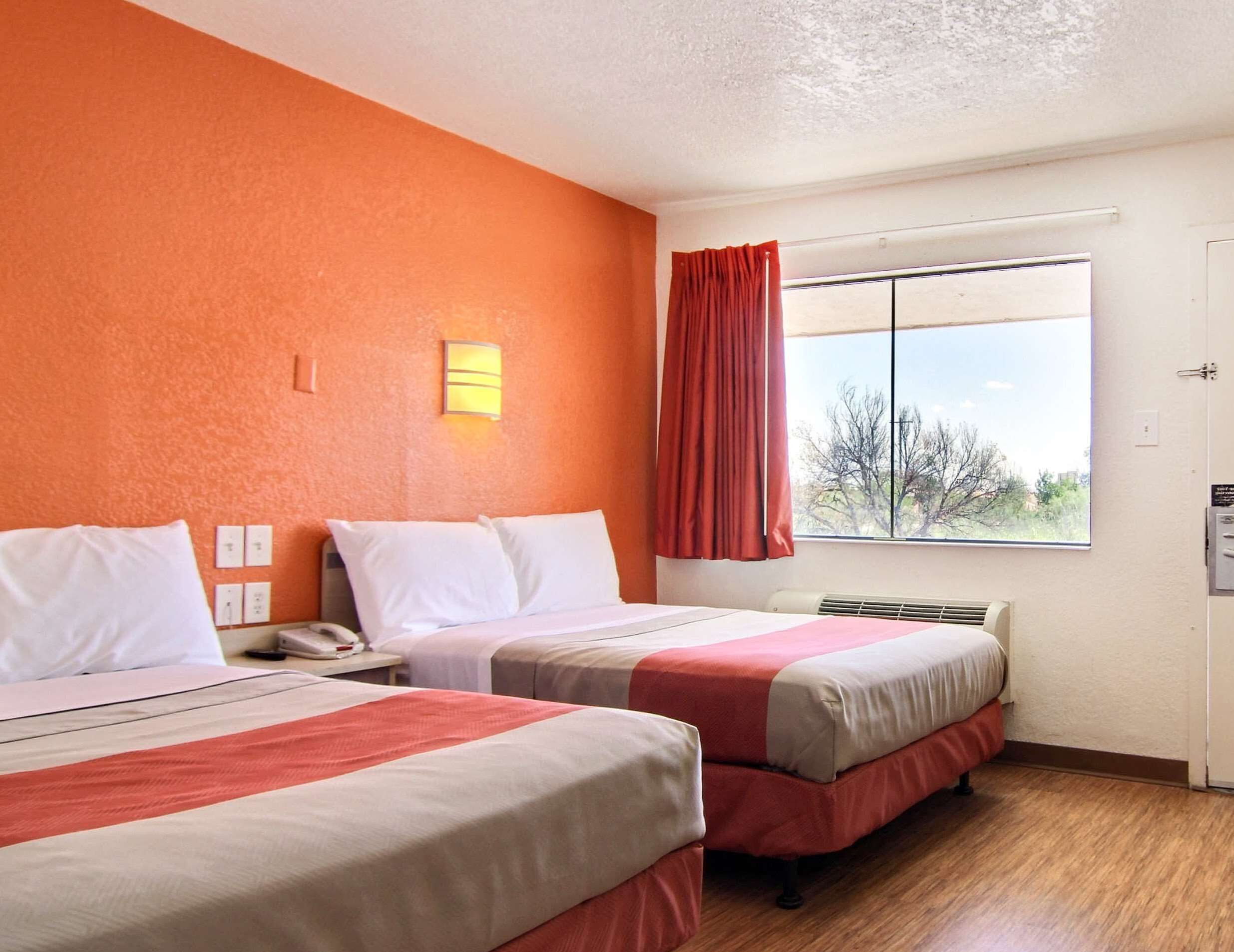 Ett hotellrum med två sängar, ett fönster med utsikt, en väggmonterad lampa och en termostat.